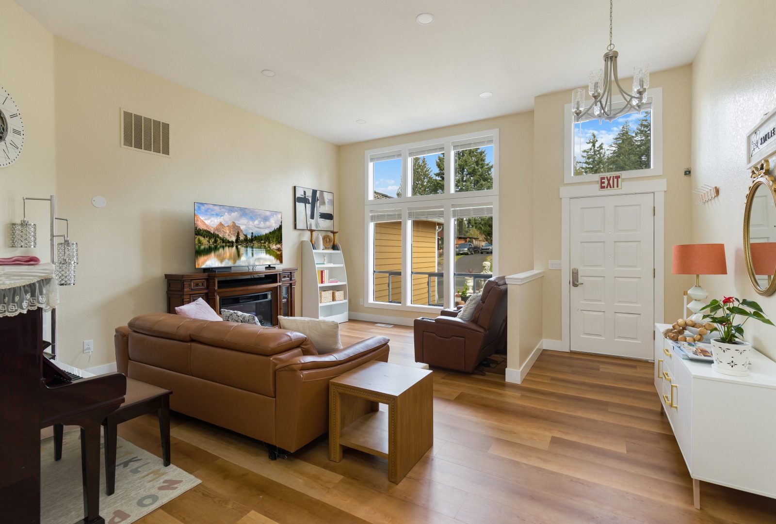 The bright living room with a leather sofa, a recliner and tall windows onto the front garden.